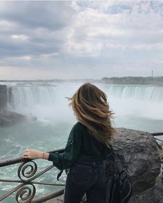 a woman standing on the side of a metal railing looking at a waterfall and water