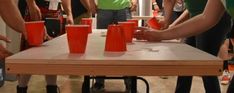 a group of people standing around a table with red cups on it and one person reaching for something