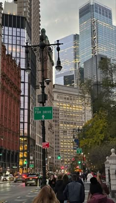 people are walking down the street in front of tall buildings and skyscrapers at dusk