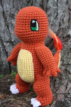 an orange crocheted stuffed animal sitting next to a tree