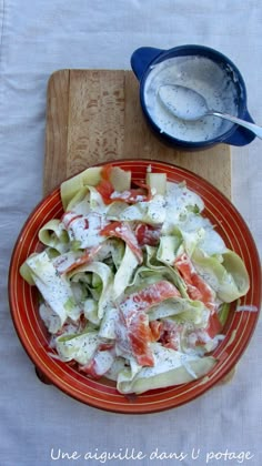 a bowl of salad with dressing next to it on a cutting board