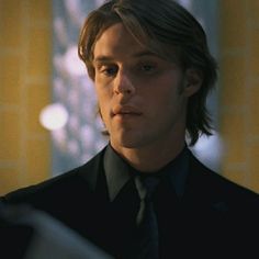 a young man in a suit and tie looking at something on his hand while standing next to a window