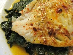 a white plate topped with fish and spinach on top of a sauce covered dish