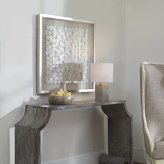 a table with a vase and some fruit on it in front of a wall mounted art piece