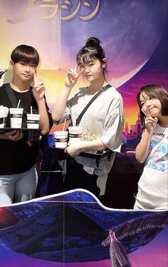 three young people standing next to each other in front of a sign with food on it