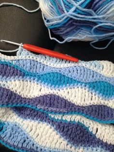 a crocheted blue and white blanket next to a ball of yarn with a red needle