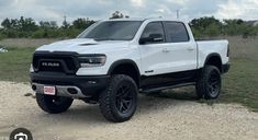 a white ram truck parked on top of a dirt road next to grass and trees