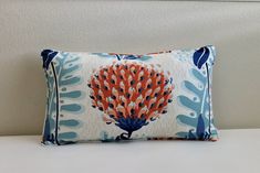 an orange and blue pillow sitting on top of a bed next to a white wall