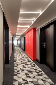 an empty hallway with black and white flooring next to red doors on either side