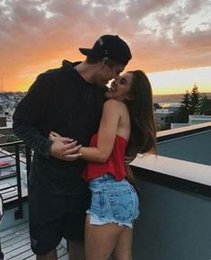 a man and woman kissing on top of a roof with the sun setting in the background