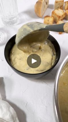 a bowl filled with soup next to bread on a white tablecloth and utensils