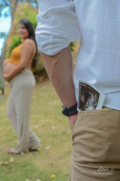 a man and woman standing next to each other in the grass with their hands on his hips