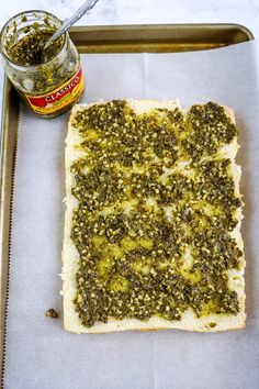 a piece of bread with pesto on it and a jar of seasoning next to it