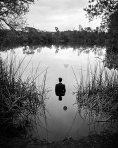 a black and white photo of a person sitting in the middle of a body of water