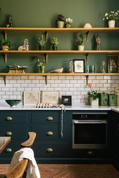 a kitchen with green cabinets and white subway tile backsplash, black countertops, and wooden shelves