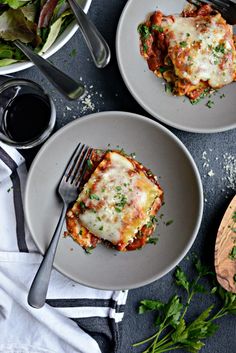 two plates with lasagna on them next to a bowl of salad and a fork