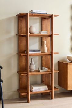 a wooden shelf with books and vases sitting on it's sides in front of a wall