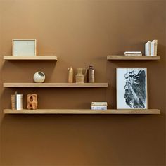 three wooden shelves with books, vases and other items on them against a brown wall