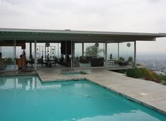 an outdoor swimming pool in front of a house with glass walls overlooking the city below