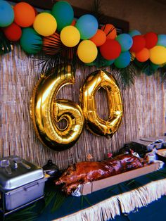 a table topped with balloons next to a large number 60 sign and a roasting pan