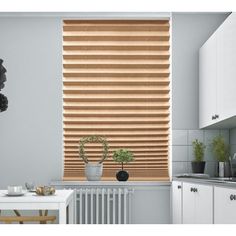 a kitchen with white cabinets and wooden blinds on the window sill, along with a potted plant