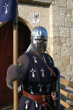 a man dressed in armor standing next to a wooden fence with a shield on his head