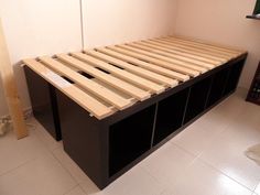 a bed frame made out of wooden slats in a room with white tile flooring