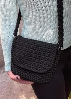 a woman is holding a black crocheted purse