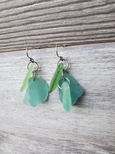 two sea glass pieces hanging from hooks on a wooden surface, one is green and the other is blue