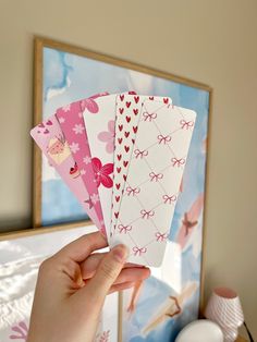 a hand holding four cards in front of a wall with pictures on the wall behind it