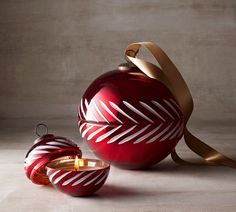 a red christmas ornament with a gold ribbon around it and two ornaments on the ground