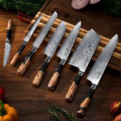 five knives are sitting on a cutting board next to some vegetables and fruit, with one knife in the middle