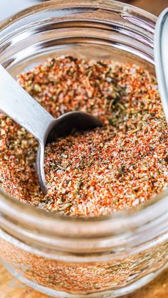 a glass jar filled with spices on top of a wooden table next to a spoon