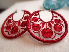 red and white embroidered hoop earrings with flower details on them, sitting on a piece of fabric