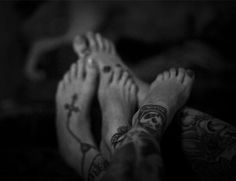 black and white photograph of two people with tattoos on their feet, one holding the other's hand