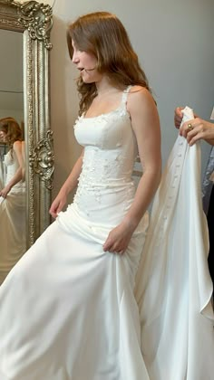 a woman in a white wedding dress is looking at herself in the mirror and holding her jacket