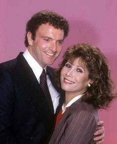 the man and woman are posing for a photo together in front of a pink background