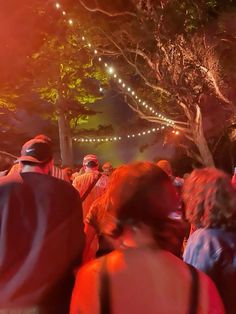 a group of people standing around each other at a party with lights and trees in the background