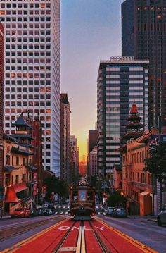 a train traveling through a city with tall buildings in the backgroung and red carpet on the ground