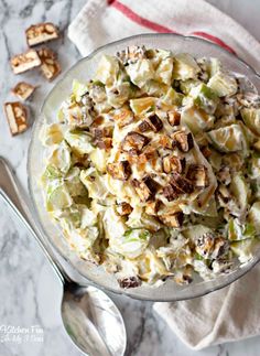 a glass bowl filled with pasta salad next to two spoons on a marble surface