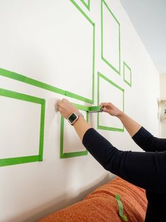 a woman is using tape to paint the wall in her bedroom with green squares on it