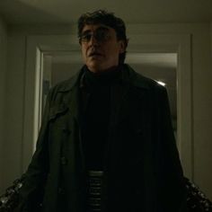 a man in a black coat and glasses standing in front of a door with his hands on his hips