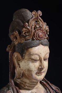 a close up of a buddha statue wearing a crown on it's head, with eyes closed