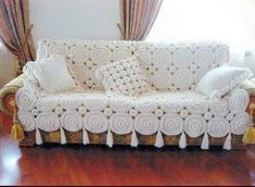 a couch covered in white crochet with tassels on the arms and back