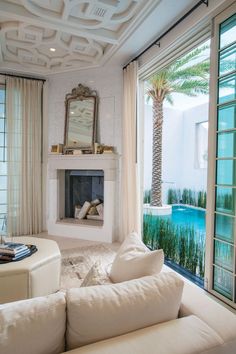 a living room with white couches and a fireplace in the corner near large windows