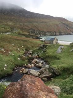 a stream running through a lush green hillside next to a small house on top of a hill