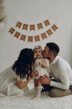 a man and woman holding a baby in front of a happy birthday bunting banner