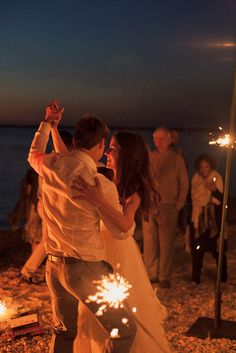 a bride and groom dancing on the beach with sparklers