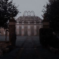 an iron gate in front of a large brick building on a foggy day with trees and bushes