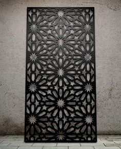 an intricately designed metal screen on the ground in front of a concrete wall with white tiles